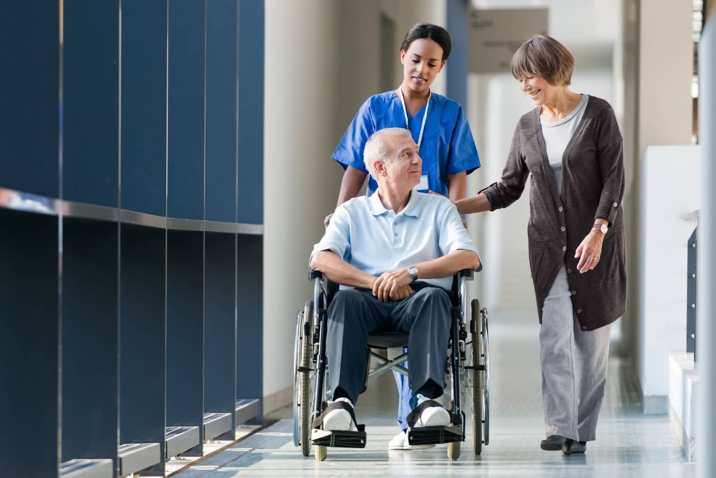 Senior Couple And Nurse Walking A Hospital Corridor